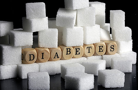 Das Foto ist ein Symbolbild für die Krankheit Diabetes, es zeigt den Begriff ausgeschrieben auf Holzwürfelchen in einem Berg von Zuckerwürfeln