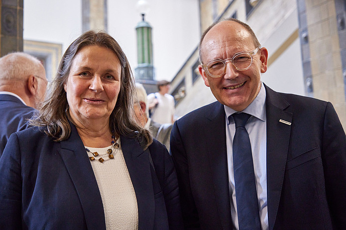 Frau in blauen Blazer steht neben Mann mit Brille