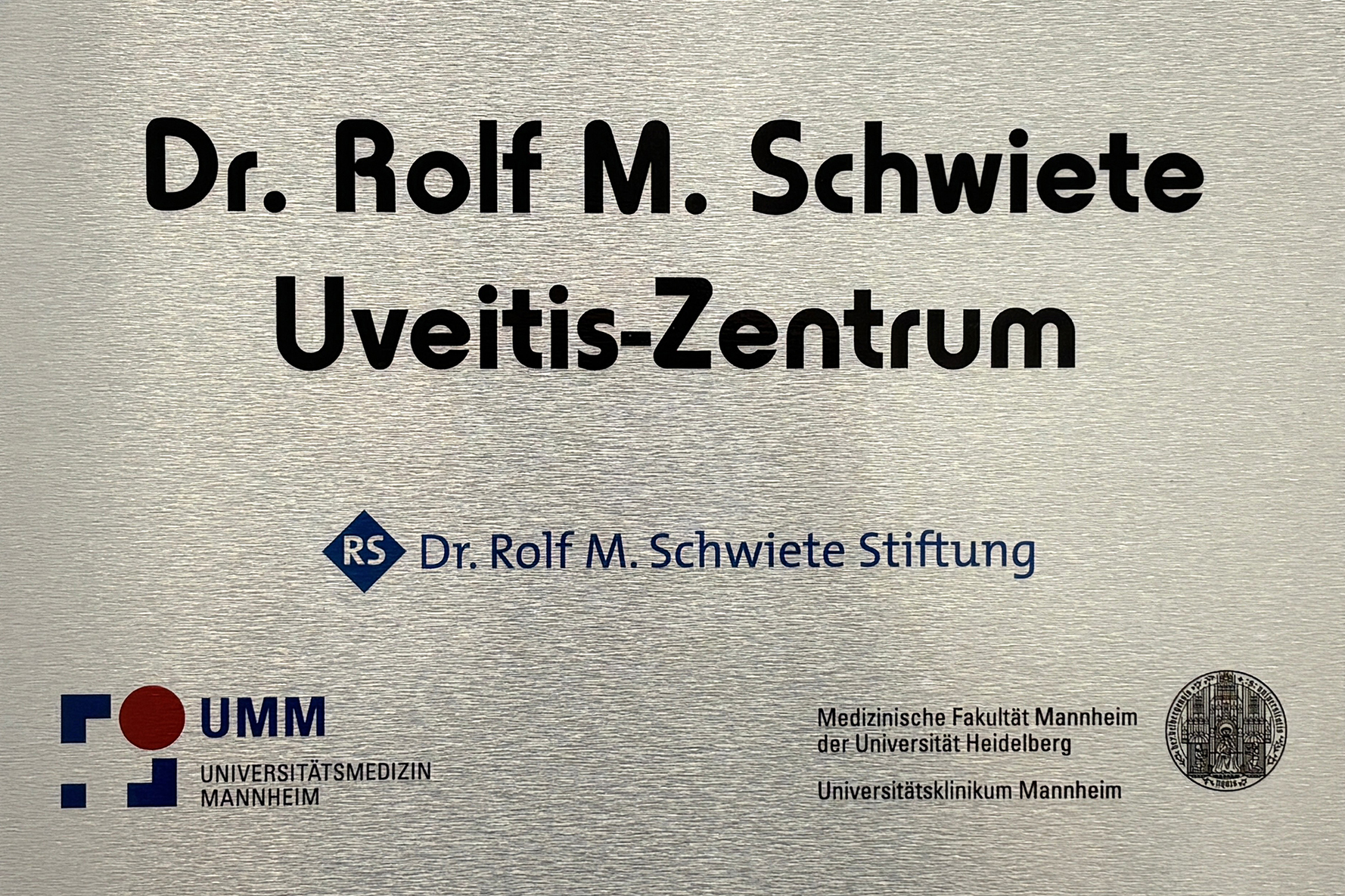 Das Bild zeigt das metallene Schild des Dr. Rolf M. Schwiete Uveitis-Zentrums 