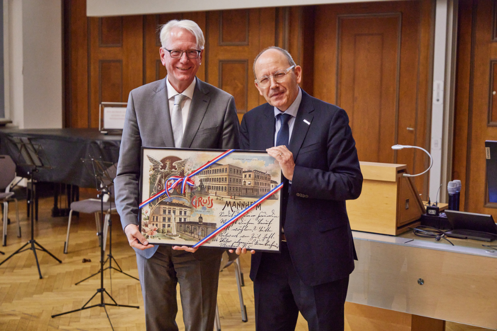 Zwei Männer halten vergrößerte historische Postkarte von Mannheim in den Händen und lächeln